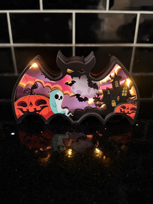 Illuminated bat-shaped Halloween decoration with pumpkins, ghosts and a haunted house